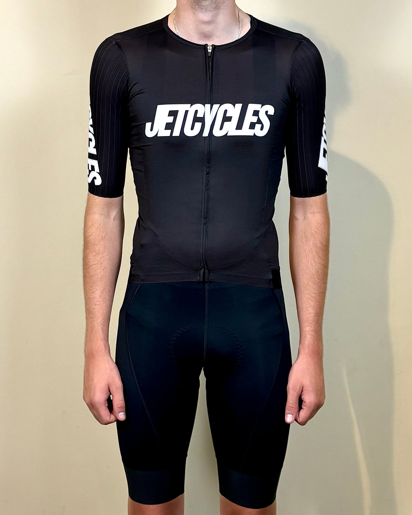 Person wearing a black cycling outfit with 'JETCYCLES' branding on a beige background