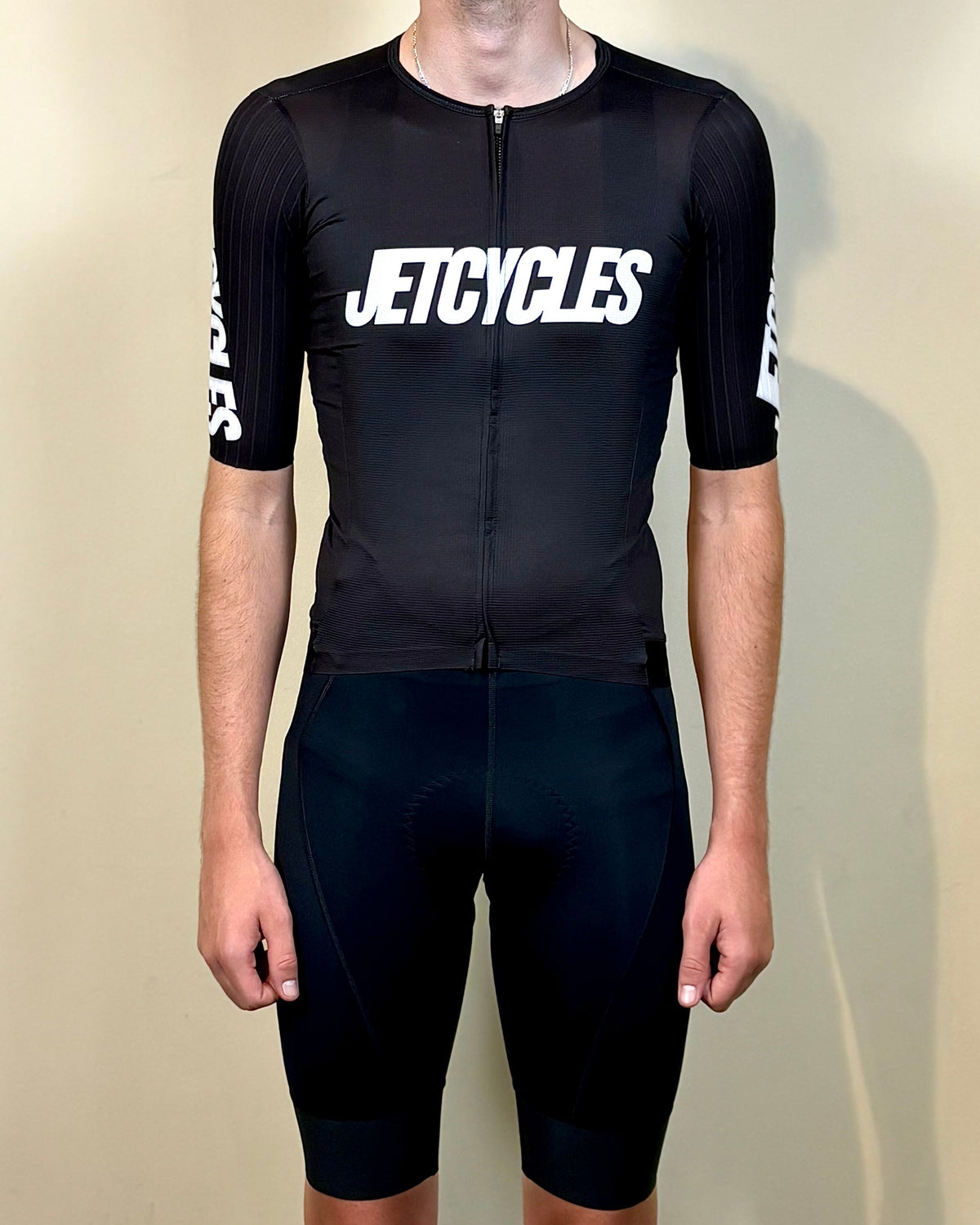 Person wearing a black cycling outfit with 'JETCYCLES' branding on a beige background